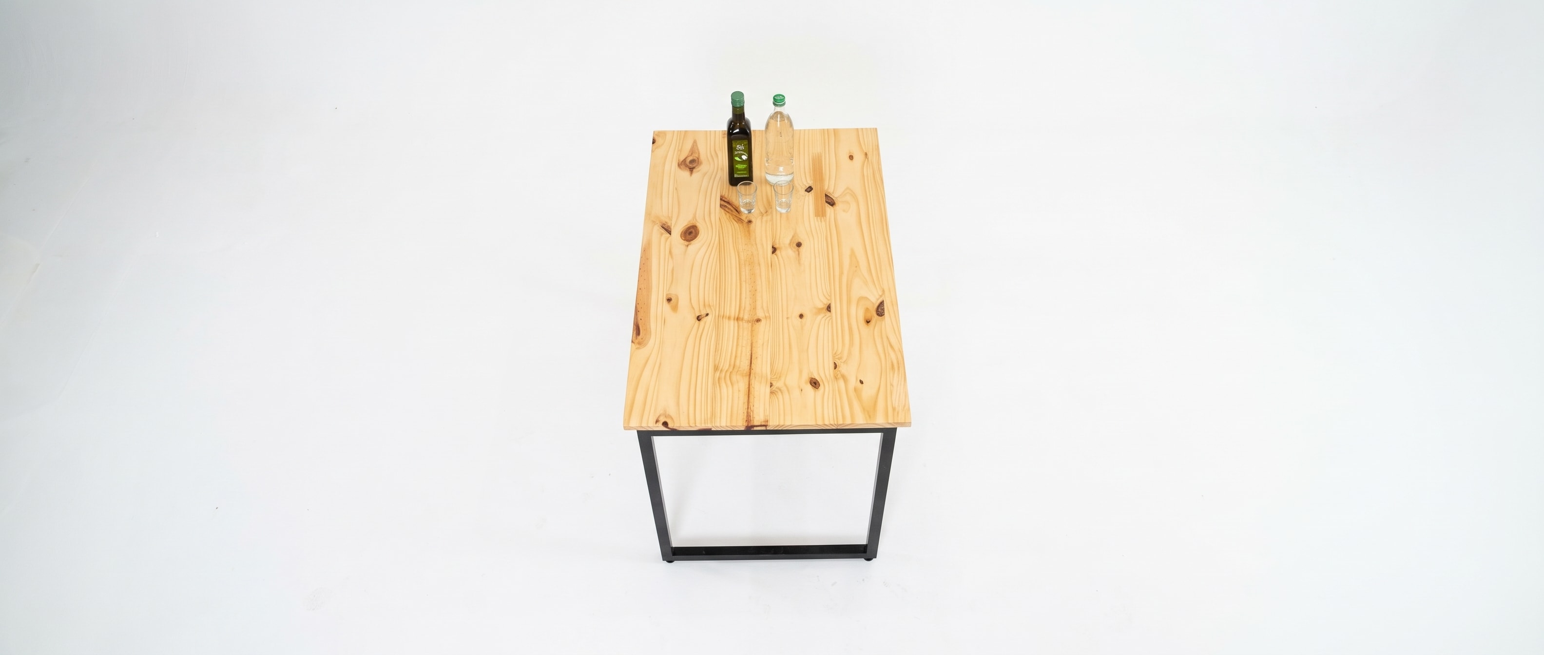 Mesa de pinho vista de cima, com azeite, água e dois copos, sobre o chão branco.